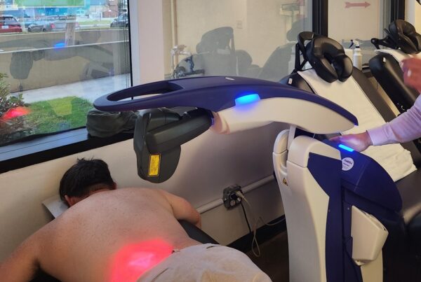 A patient receives laser therapy on their lower back while lying face down in a chiropractic clinic. - Herniated Disc