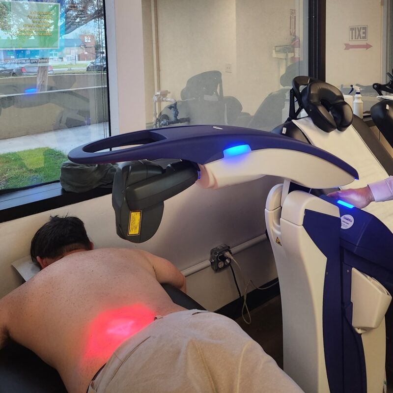 A patient receives laser therapy on their lower back while lying face down in a chiropractic clinic. - Herniated Disc