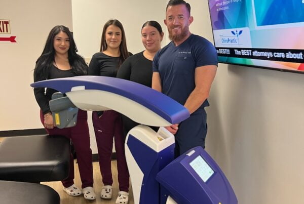 A group of four people stands beside a laser therapy machine in a chiropractic clinic. - Laser Therapy
