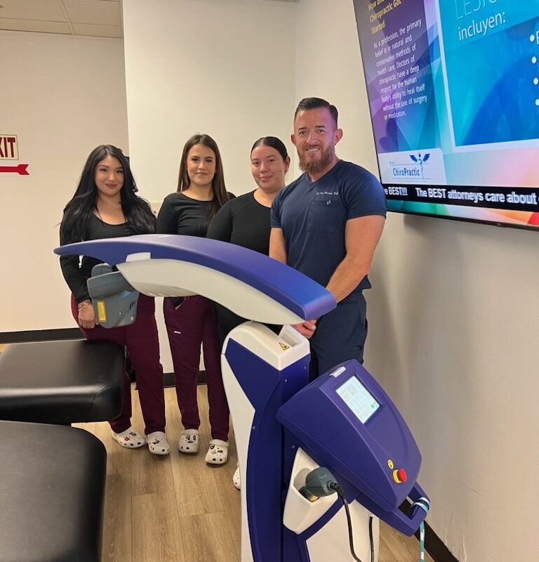 A group of four people stands beside a laser therapy machine in a chiropractic clinic. - Laser Therapy