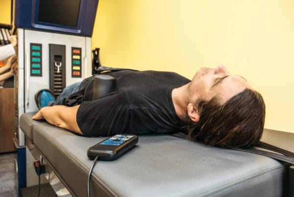 A person lies on a specialized table receiving spinal decompression therapy. - Spinal Decompression