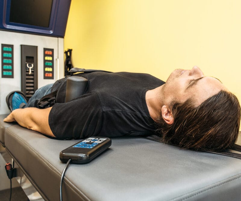 A person lies on a specialized table receiving spinal decompression therapy. - Spinal Decompression